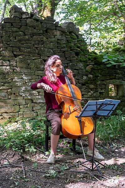Cellistin spielt vor einer Ruine im Wald