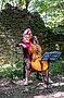 Cellistin spielt vor einer Ruine im Wald
