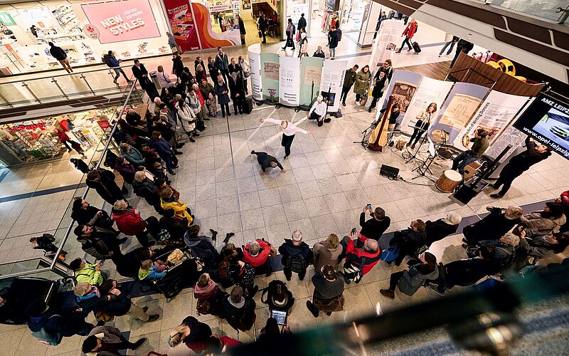 Aufnahme aus der Vogelperspektive: Viele Menschen stehen im Halbkreis, auf der anderen Seite drei Musiker, in der Mitte die Tänzer.